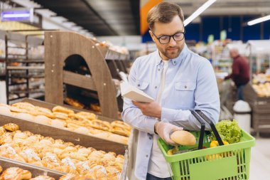 Customer wearing gloves, carefully selecting fresh bread while reading the ingredients list at a well organized supermarket bakery