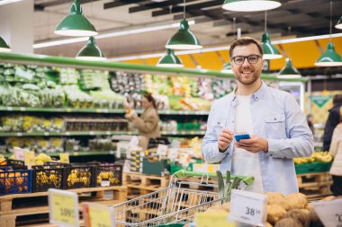 Customer taking notes on notepad while buying groceries in supermarket with full shopping cart