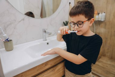 Child using electric toothbrush, promoting oral hygiene and healthy habits from a young age in a modern bathroom