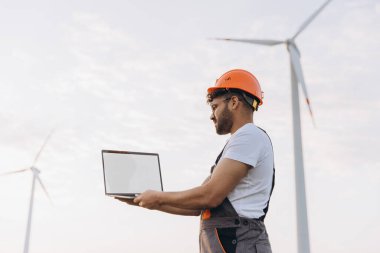 Arab engineer holding laptop analyzing wind turbines, renewable energy and eco friendly business concept
