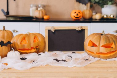 Cadılar Bayramı balkabakları ve boş karatahta mutfak masasında örümcek ağı örümcekler ve yarasa süslemeleri ile oturuyorlar.