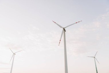 Rüzgar türbinleri bulutlu bir gökyüzüne karşı dönerek ve yenilenebilir enerji üreterek sürdürülebilir gücü ve çevreyi korumayı sembolize eder.