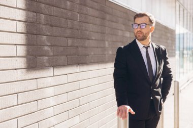 Businessman wearing suit and tie standing near a brick wall and looking away