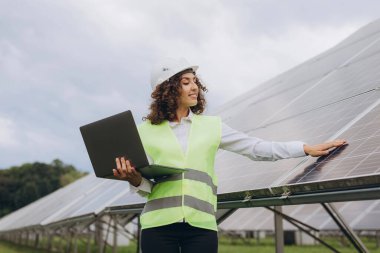 Engineer holding a laptop while inspecting solar panels in a vibrant solar farm, contributing to renewable energy and sustainability efforts