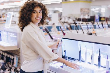 Customer comparing electric toothbrushes in electronics store, selecting best option for oral hygiene