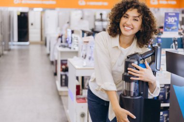 Smiling woman selecting cordless vacuum cleaner in home appliance store, showcasing consumer choice and retail experience