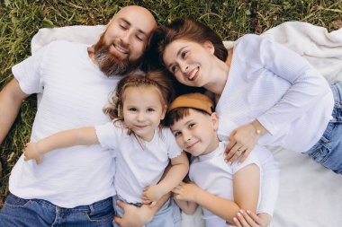 Smiling family with two children lying on a blanket in a park, enjoying their leisure time together