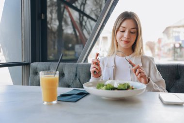 Young woman enjoying a fresh salad with mozzarella cheese while sipping orange juice in a vibrant restaurant setting