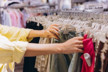 Customer browsing through an array of clothes on hangers in a clothing store, engaging in the shopping and retail experience