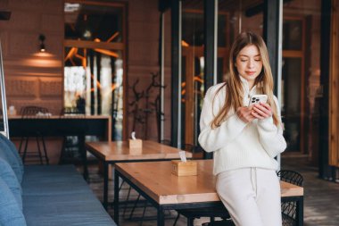 Casual dressed woman using her smartphone in a modern cafe, enjoying a moment of relaxation and connection