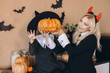 Mother and daughter dressed in costumes, joyfully preparing a carved pumpkin for their festive Halloween party celebration