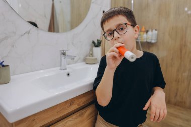 Child using electric toothbrush, promoting oral hygiene and healthy habits in a modern bathroom setting