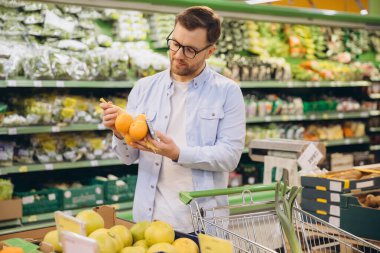 Customer buying oranges in grocery store, holding a net of oranges in his hands