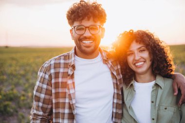 Two agronomists hugging and smiling in a soybean field at sunset, enjoying the fruits of their labor