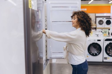 Customer opening the refrigerator door, selecting a new fridge while browsing through options in a modern electronics store
