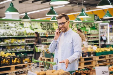 Customer choosing potatoes while using mobile phone in grocery store