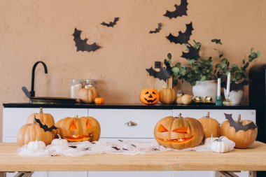 Pumpkins carved with spooky faces illuminate a kitchen table decorated for Halloween, creating a warm and festive atmosphere