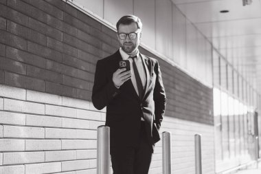 Businessman reading messages on smartphone while walking near office