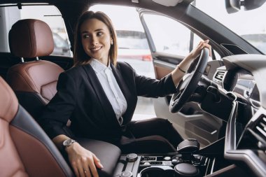 Businesswoman sitting in driver's seat of new car, holding steering wheel and smiling