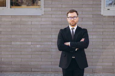Portrait of a successful businessman standing with arms crossed in front of a modern office building, conveying confidence and professionalism