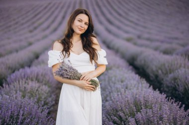 Young woman wearing a flowing white dress, holding a fragrant bouquet of lavender while surrounded by a stunning lavender field in full bloom