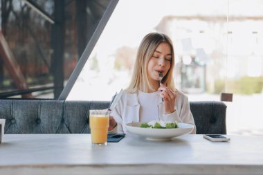 Young woman enjoying a fresh salad and sipping on orange juice while taking a break at a modern restaurant during her busy lunch hour