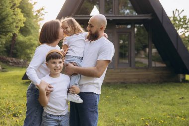 Smiling family enjoying a sunny day in the garden of their new a frame house, celebrating togetherness and happiness in their cozy home