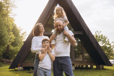 Smiling family standing outside their new a frame house, enjoying the sunlight and fresh air of the countryside