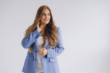 Studio portrait of a confident young businesswoman adjusting her blue jacket while smiling and looking away