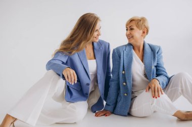 Businesswomen mother and daughter wearing blue jackets and white trousers are sitting on the floor talking and smiling