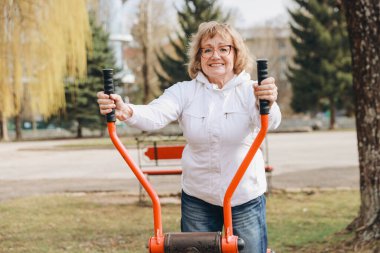 Elderly woman exercising on outdoor gym equipment, promoting healthy lifestyle and active aging in a park setting