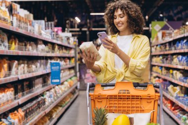 Customer comparing products information using a smartphone app while grocery shopping in a supermarket