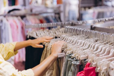 Customer browsing through a variety of clothes on hangers in a retail store, carefully choosing garments for her wardrobe