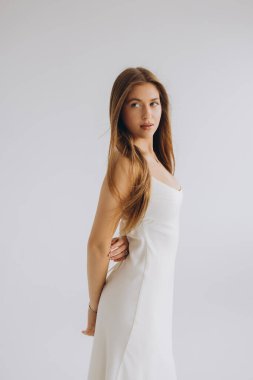 Fashion model posing in elegant white dress with long hair, looking over her shoulder against a minimalist white background