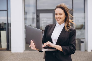 Smiling saleswoman using laptop in front of car dealership