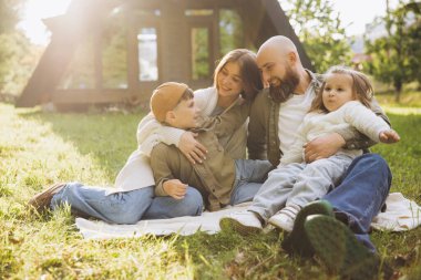 Family sitting on a cozy blanket in the backyard, enjoying quality time together, sharing laughter and creating joyful memories in the sunlight