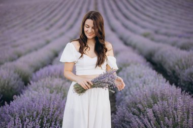 Model dressed in elegant white clothing, holding a vibrant lavender bouquet while surrounded by a picturesque lavender field in full bloom