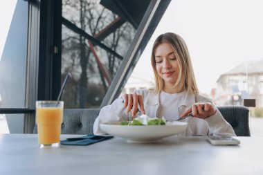 Young blond woman enjoying a healthy meal of fresh salad and orange juice in a modern restaurant