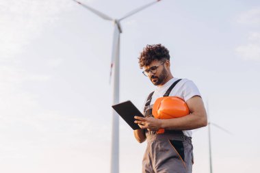 Arab engineer using digital tablet working near wind turbine for renewable and sustainable energy