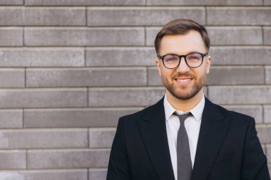 Portrait of a businessman smiling in front of a brick wall, wearing glasses and a suit