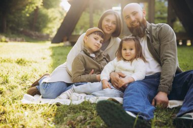 Smiling family relaxing together on a blanket in a park, enjoying quality time surrounded by nature and creating joyful memories
