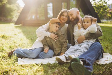 Smiling family sitting on a blanket in a park, enjoying a delightful picnic under the warm sun, surrounded by nature and laughter