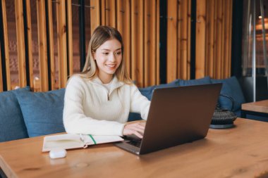 Smiling woman working remotely on a laptop in a cozy cafe, enjoying the blend of comfort and productivity in a modern setting