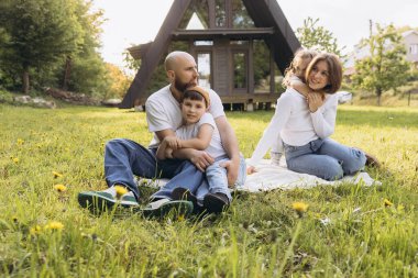 Happy family relaxing on grass in front of their a frame country house, enjoying quality time together