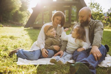 Happy family having fun together sitting on a blanket in the backyard of their house during a sunny day