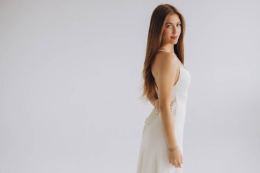Fashion model posing gracefully in a studio, showcasing an elegant white dress that highlights beauty and contemporary style