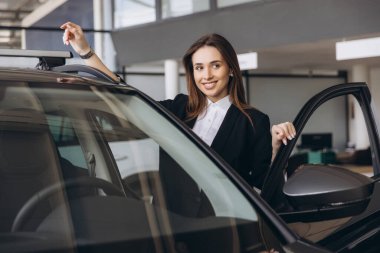Smiling saleswoman engaging with a customer while highlighting the roof rack of a new car in a modern dealership showroom