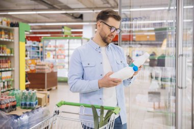 Man choosing fresh milk bottles while shopping in supermarket refrigerator aisle