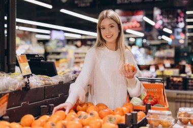 Müşteri elinde bir alışveriş sepeti tutarken canlı bir marketten taze hurma seçiyor, sağlıklı ürünlerin bolluğunun tadını çıkarıyor.