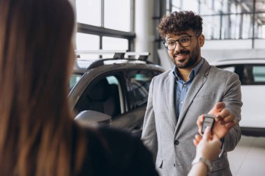 Car salesman handing over keys to a delighted female customer, celebrating the excitement of purchasing a new car in a modern dealership showroom